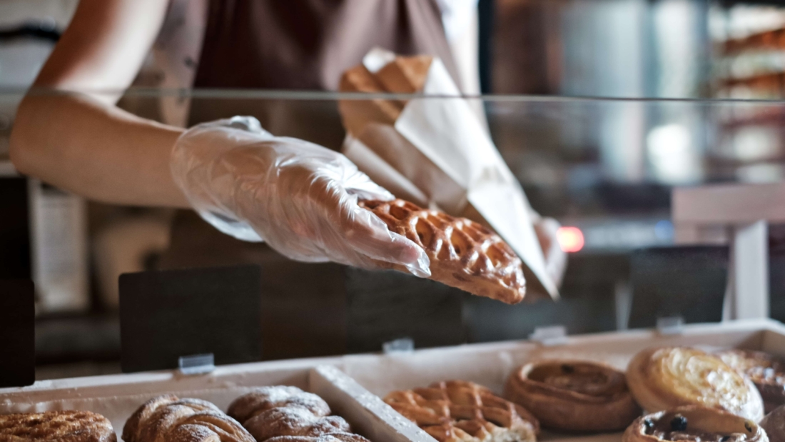 European woman sells in bakery putting bread in paper bag. Small business concept