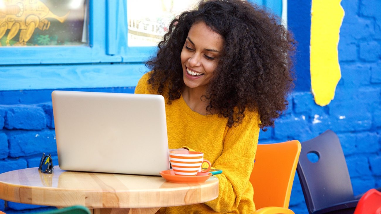 happy-young-woman-sitting-at-outdoor-cafe-using-PFFBJ93