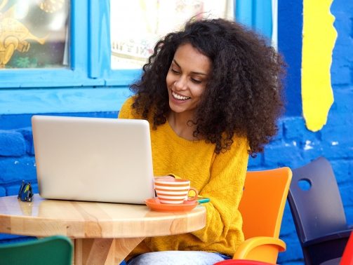 happy-young-woman-sitting-at-outdoor-cafe-using-PFFBJ93