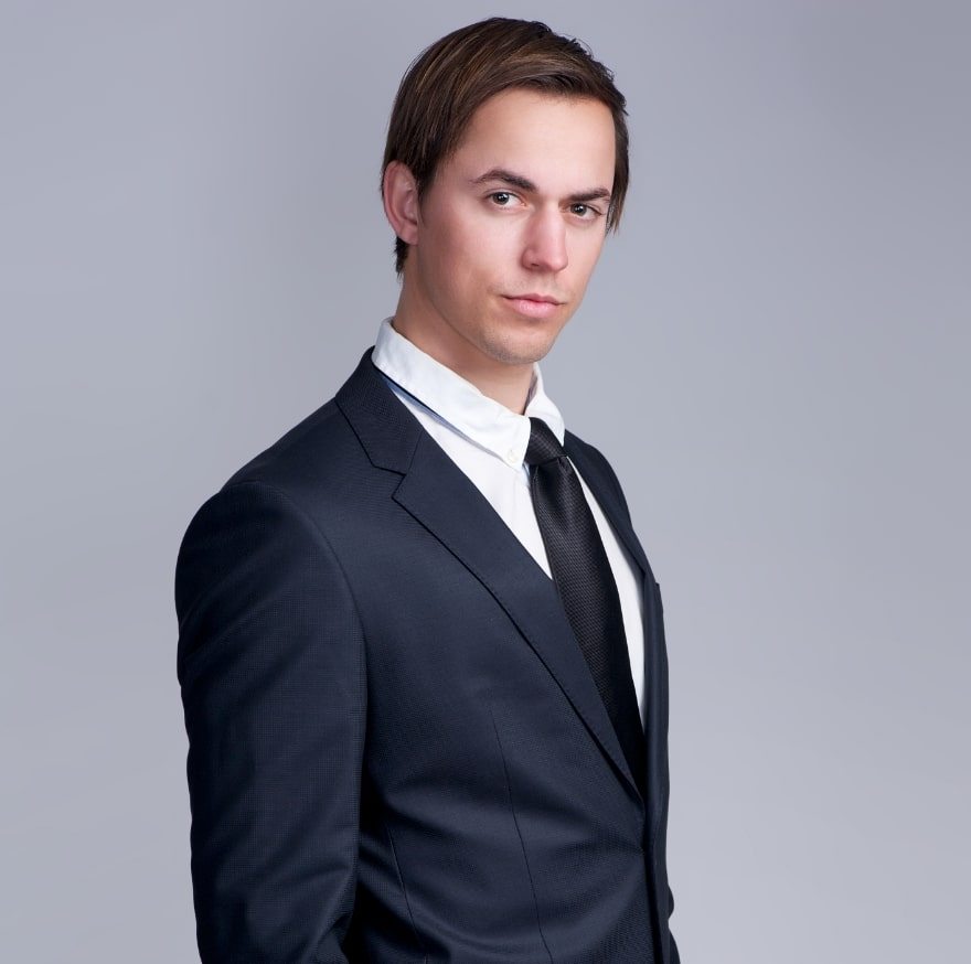 handsome-young-businessman-standing-against-gray-PFGZN4E-min