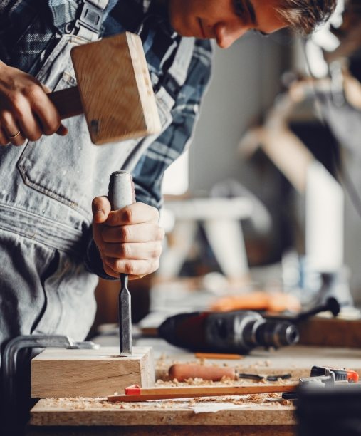 A man carves a tree. The carpenter works with a hammer in a studio. An engineer provides a tree shape
