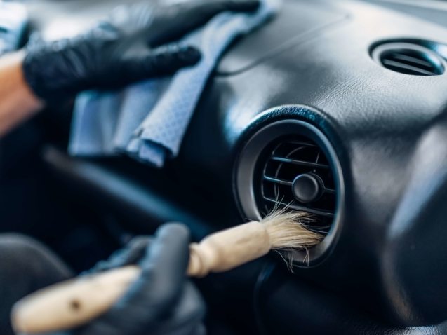 Auto detailing of car interior on carwash service. Worker in gloves cleans salon with brush