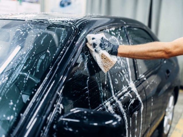 Carwash service, car cleaning, front view. Auto detailing, worker soaps glasses