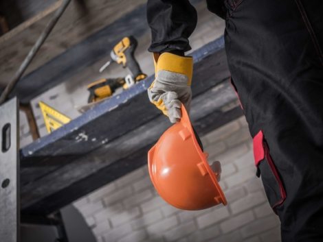 Hard Hat Construction Zone. Contractor with Orange Safety Hard Hat in Hand. Scaffolding with Tools in Background.