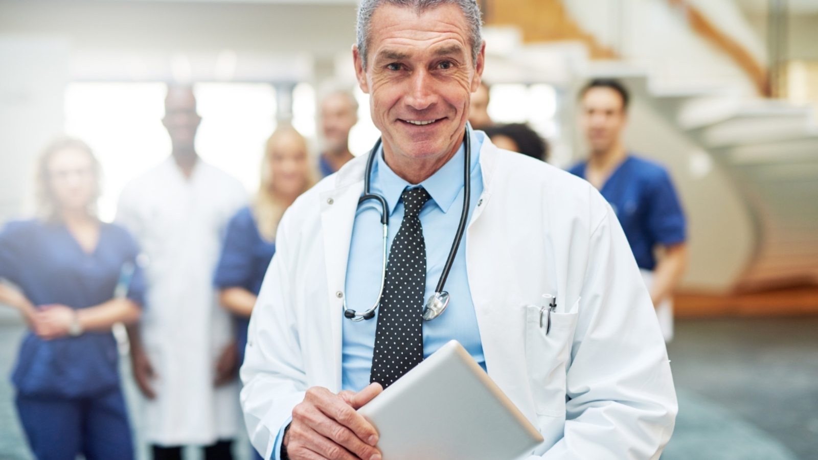 cheerful-mature-doctor-with-tablet-in-hospital-UW72G9C