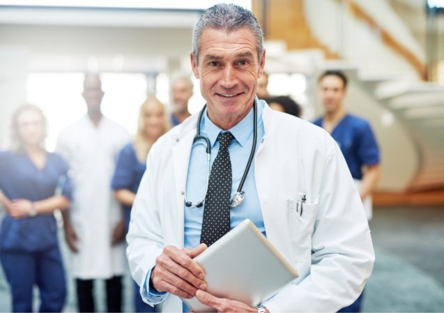 cheerful-mature-doctor-with-tablet-in-hospital-UW72G9C