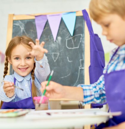 Portrait of adorable little girl  painting pictures enjoying art class in pre school working together with other kids