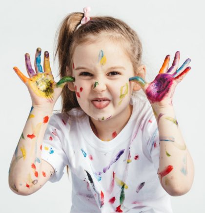 Little girl covered in paint making funny faces. Kindergarten kid. Prankster.