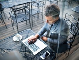 mature-businessman-with-laptop-outside-a-cafe-PXAVBAC