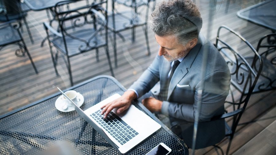 mature-businessman-with-laptop-outside-a-cafe-PXAVBAC