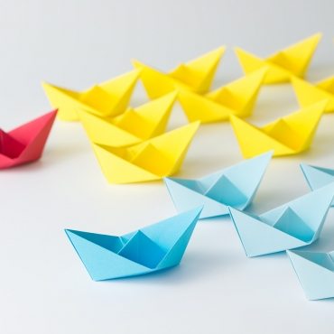 Business competition concept using two different color origami paper boats