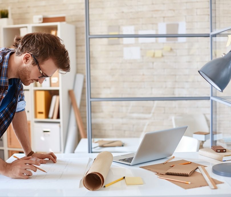 Modern architect looking at blueprint with sketch of construction in office