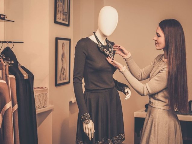young-woman-looking-at-necklace-on-mannequin-in-PSQQMMH