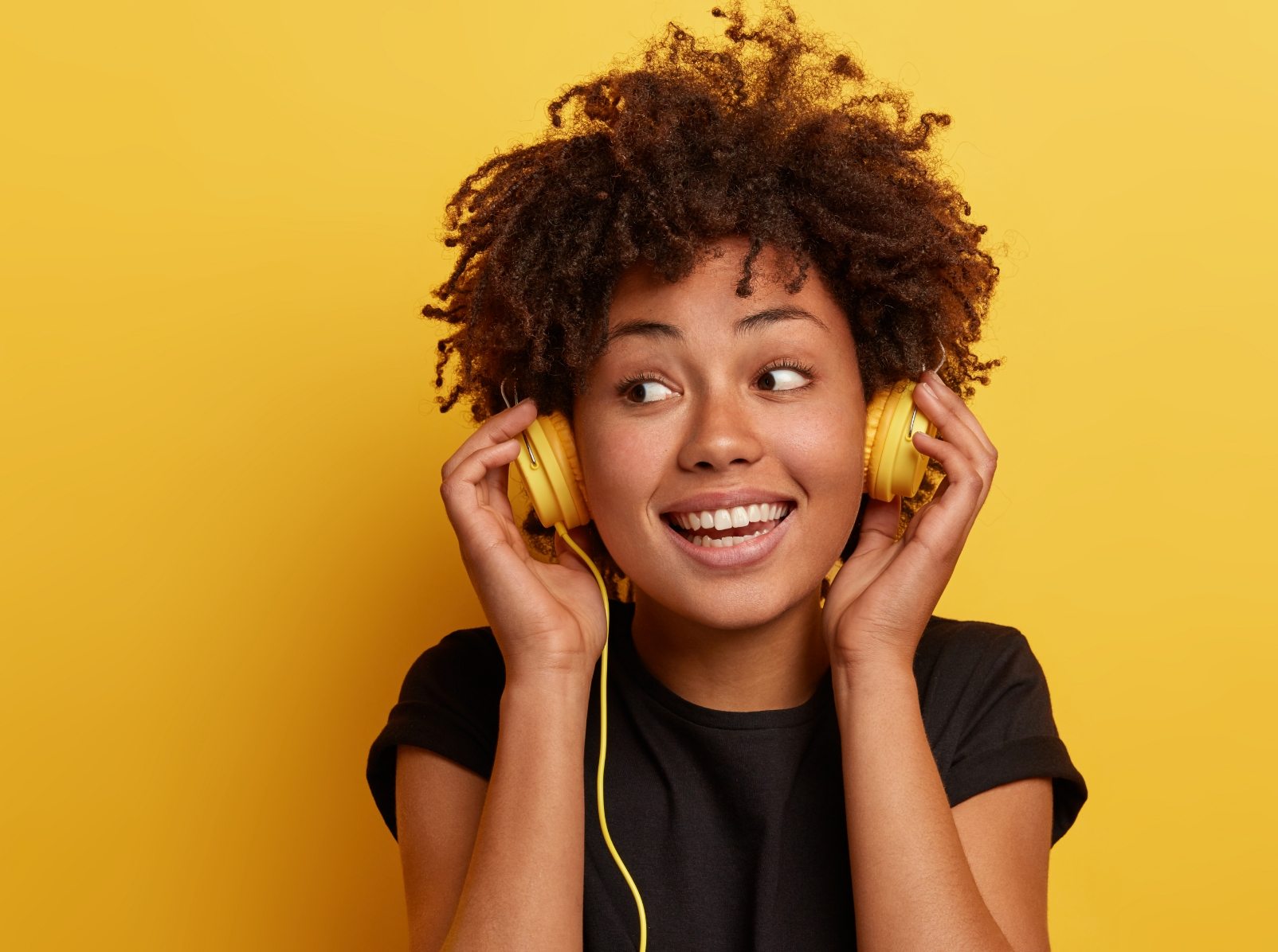 happy-dark-skinned-woman-wears-wired-headphones-enjoys-nice-music-looks-away-has-toothy-smile
