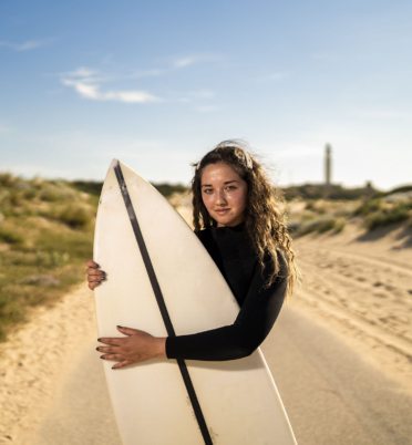 A shallow focus shot of an attractive female hugging a surfboard in the middle of the road in Spain